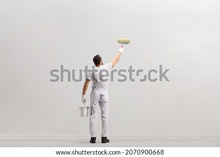 Rear view shot of a painter holding a bucket and painting a wall isolated on white background