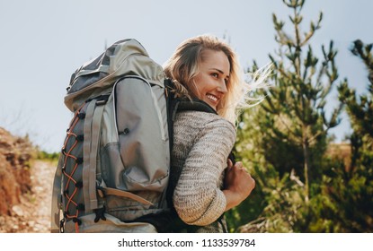 Rear view shot of smiling woman with backpack going on a camping. Caucasian female hiker on mountain looking away and smiling. - Powered by Shutterstock