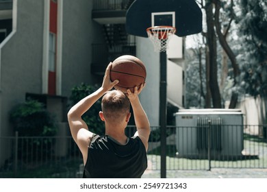 Rear view shot of a streetball player shoots basketball. Young guy playing basketball on outdoor court on a summer day. High quality photo - Powered by Shutterstock