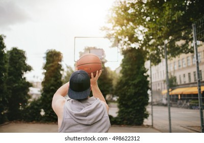 Rear view shot of a young guy playing basketball on outdoor court. Streetball player shoots basket. - Powered by Shutterstock