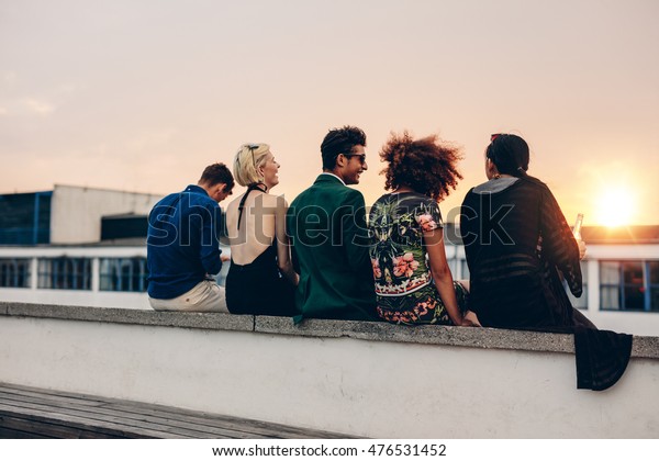 若い男性と女性が屋上で一緒に座っている様子を撮影した写真 夕日の間にテラスでくつろぐ人種の交流の友達 の写真素材 今すぐ編集