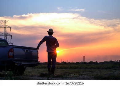 Rear view of silhouette farmer in farmland, looking at sunset, traveling by pickup truck in countryside