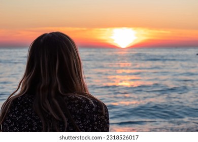 Rear view of Silhouette of woman on Sveti Stefan sand beach with scenic romantic view of sunset at horizon of Adriatic Mediterranean Sea, Budva Riviera, Montenegro, Europe. Summer vacation at seaside