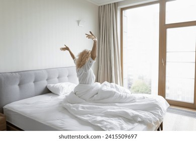 Rear view of single blonde female wakes up in bed stretching body with arms raised, feels good and refreshed in cozy bedroom. Orthopaedic mattress for comfortable night sleep, healthy rest, new day - Powered by Shutterstock