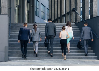 Rear View Of Six Business People Walking Up The Stairs. Men And Women In Formal Suits Going Up Stairs Into Office Building. Partnership, Communication Business People Concept.