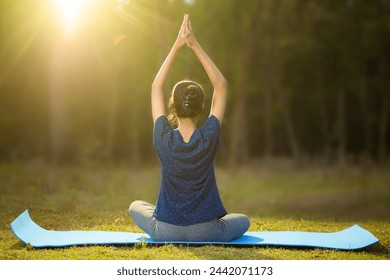 rear view of an slim women sitting in a sukhasana pose doing prayer pose yoga by facing towards morning sunrise - Powered by Shutterstock