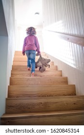 A Rear View Of Small Girl Walking Up Wooden Stairs Indoors At Home.