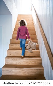 A Rear View Of Small Girl Walking Up Wooden Stairs Indoors At Home.