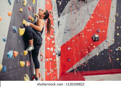 Rear view of sportwoman climber moving up on steep rock, climbing on artificial wall indoors. Extreme sports and bouldering concept.