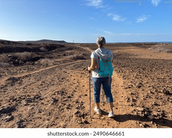 Rear view of a sporty senior woman outdoors on a sunny day walking along a coastal path towards a lighthouse, peaceful and healthy retired lifestyle - Powered by Shutterstock