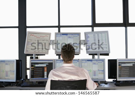 Rear view of stock trader looking at multiple computer screens