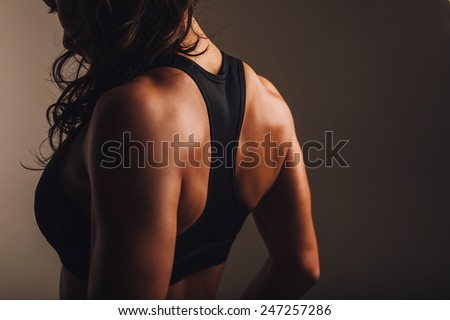 Rear view of strong young woman wearing sports bra. Muscular back of a woman in sportswear.