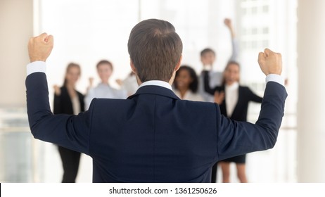Rear view at successful company ceo celebrating business win victory success with corporate team in office, back of leader manager with hands raised overjoyed by work goal achievement reward growth
