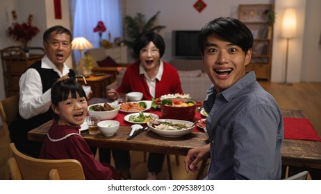 rear view surprised asian father and daughter turning to look at camera with other family members, showing wonder as someone walking near dinner table with delicious food