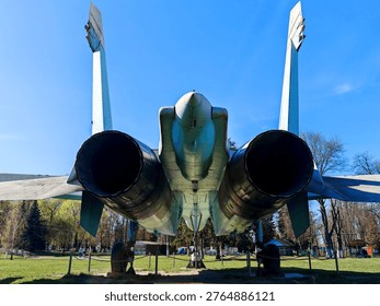A rear view of the tail section of a Soviet Su-27 fighter jet, showing the two massive jet engine nozzles, the center boom, and the two vertical stabilizers.