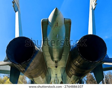 A rear view of the tail section of a Soviet Su-27 fighter jet, showing the two massive jet engine nozzles, the center boom, and the two vertical stabilizers.