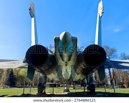 A rear view of the tail section of a Soviet Su-27 fighter jet, showing the two massive jet engine nozzles, the center boom, and the two vertical stabilizers.
