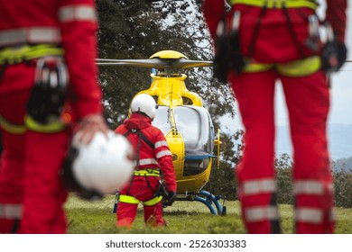 Rear view of team of emergency medical service. Doctor and paramedics with safety harness and climbing equipment running to helicopter. Themes rescue, help and hope.
