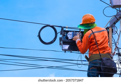 Rear view of technician on wooden ladder checking code numbers of  fiber optic cable lines in internet splitter box for repairing to work normally on electric pole against blue sky background