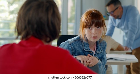 Rear view of teen girl student turn back and talk to classmate sitting at desk on classroom. Teenage schoolchildren communicate during lesson - Shutterstock ID 2063526077