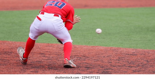 Rear view of the third baseman fielding a ball during a high school baseball game on a green and red turf field.