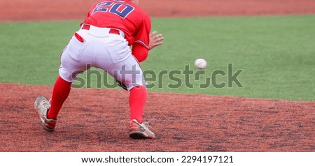 Rear view of the third baseman fielding a ball during a high school baseball game on a green and red turf field.