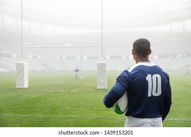 Rear view of thoughtful African american male rugby player standing with rugby ball in stadium - Powered by Shutterstock