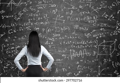 Rear view of a thoughtful woman who tries to solve math problems. Math calculations on black chalk board.