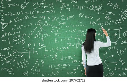 Rear View Of A Thoughtful Woman Who Is Writing Math Calculations On Green Chalk Board.