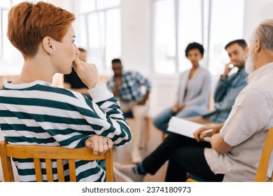 Rear view of thoughtful young woman thinking about mental problem or addiction sitting in circle during group therapy session. Concept of mental health, psychotherapy, depression, social issues. - Powered by Shutterstock