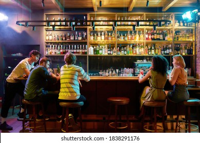 Rear view of three guys drinking beer, looking at women, two girlfriends sitting at the bar counter. Friends spending time at night club, restaurant. Horizontal shot - Powered by Shutterstock
