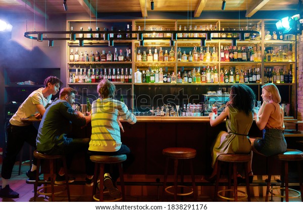 Rear view of three guys\
drinking beer, looking at women, two girlfriends sitting at the bar\
counter. Friends spending time at night club, restaurant.\
Horizontal shot