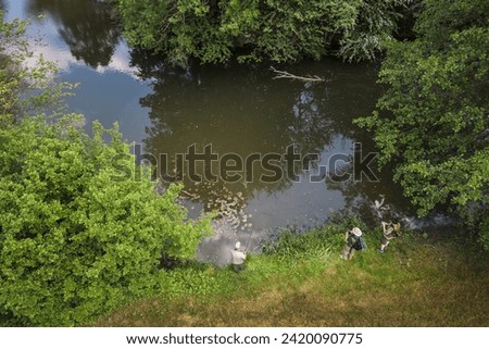 Rear view of three sports fishermen enjoying fishing in tranquil river surroundings, aerial shot. Vacation, hobby, and leisure activity concepts.