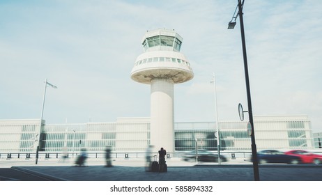 Rear View Of Tired Man With Luggage Waiting For Taxi After His Arrival In Barcelona, Silhouette Of Young Guy With Several Suitcases In Front Of Air Traffic Control Tower Of Modern Contemporary Airport