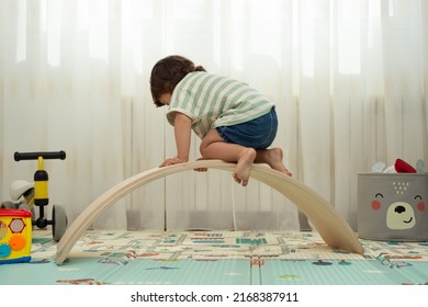 Rear View Of A Toddler Climbing On A Balance Board In A Montessori Playroom.