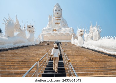 Rear view of tourist walking on the stairs in front of an iconic statue of Guanyin located in Wat Huay Pla Kang of Chiang Rai province of Thailand. Guanyin is the Chinese Goddess of Mercy.