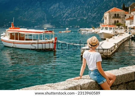 Rear view of a tourist woman sitting on a waterfront of the beatiful small town Perast, Kotor Bay, Montenegro