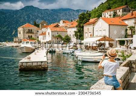 Rear view of a tourist woman taking a picture of the beatiful small town Perast on her mobile, Kotor Bay, Montenegro