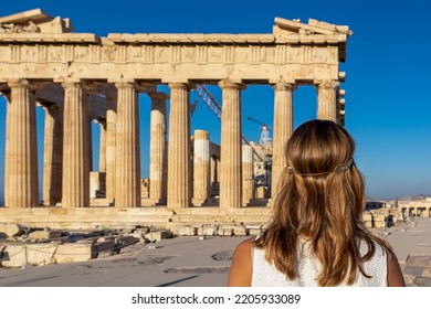 Rear View Of Tourist Woman In White Dress Looking At Parthenon Of Acropolis Of Athens, Attica, Greece, Europe. Ruins Of Ancient Temple, The Birthplace Of Democracy. Girl Wearing Golden Laurel Crown