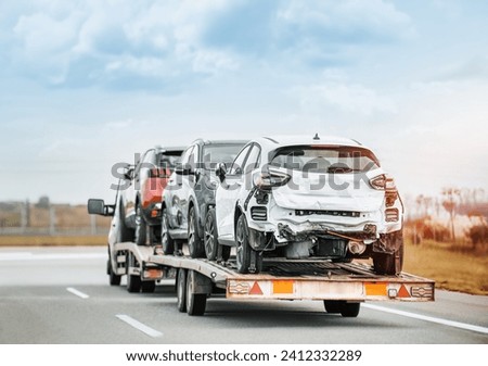 Rear view of tow truck transporting 3 totaled damaged cars. Car insurance paid off the actual cash value ACV. Car restoration after being totaled. Car auctions.