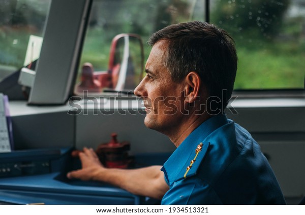 Rear view of train driver in the loco cab.\
Profile of the person driving the train. Railwayman or train crew\
in uniform near to window and control\
panel
