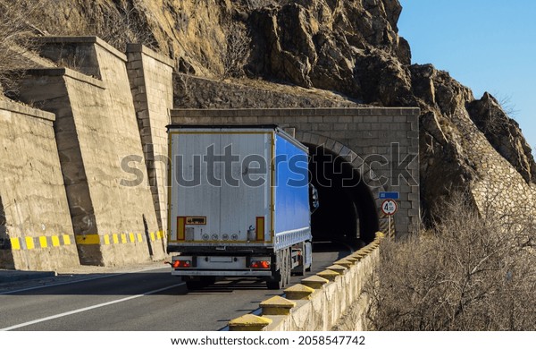 Rear view of\
truck without logo on the mountain road, at the entrance to the\
tunnel. Cargo transportation\
concept