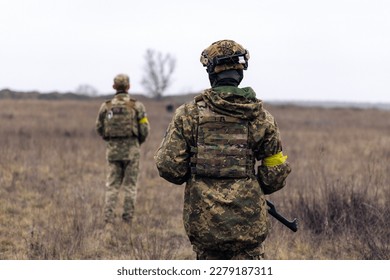 Rear view of two armed Ukrainian soldiers walking in steppe in uniform and helmets. War in Ukraine. Russian aggression and military invasion in Ukraine.