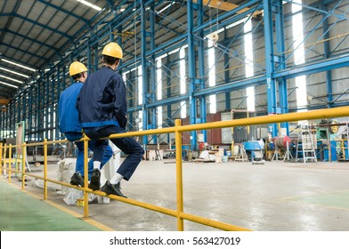 Rear view of two blue-collar workers during break in the interior of an industrial hall