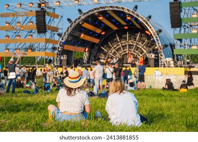 Rear view of two friends sitting on the grass, enjoying the vibe at an outdoor music festival concert. - Powered by Shutterstock