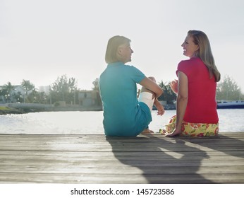 Rear View Of Two Middle Aged Women Sitting On Pier