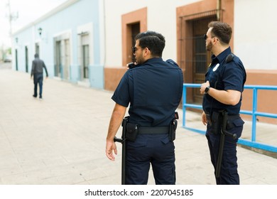 Rear View Of Two Police Cops Chasing A Suspect Criminal With A Hoodie After A Robbery In The Street 