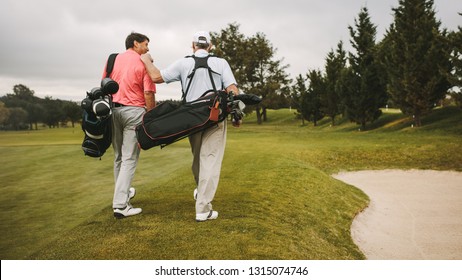 Rear view of two senior golf players walking together in the golf course with their golf bags. Senior golfers walking towards the next hole.