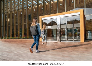 Rear view of two unrecognizable college students entering the university to attend classes on a sunny day.