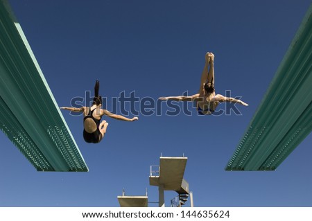 Rear view of two women diving from diving boards against clear blue sky